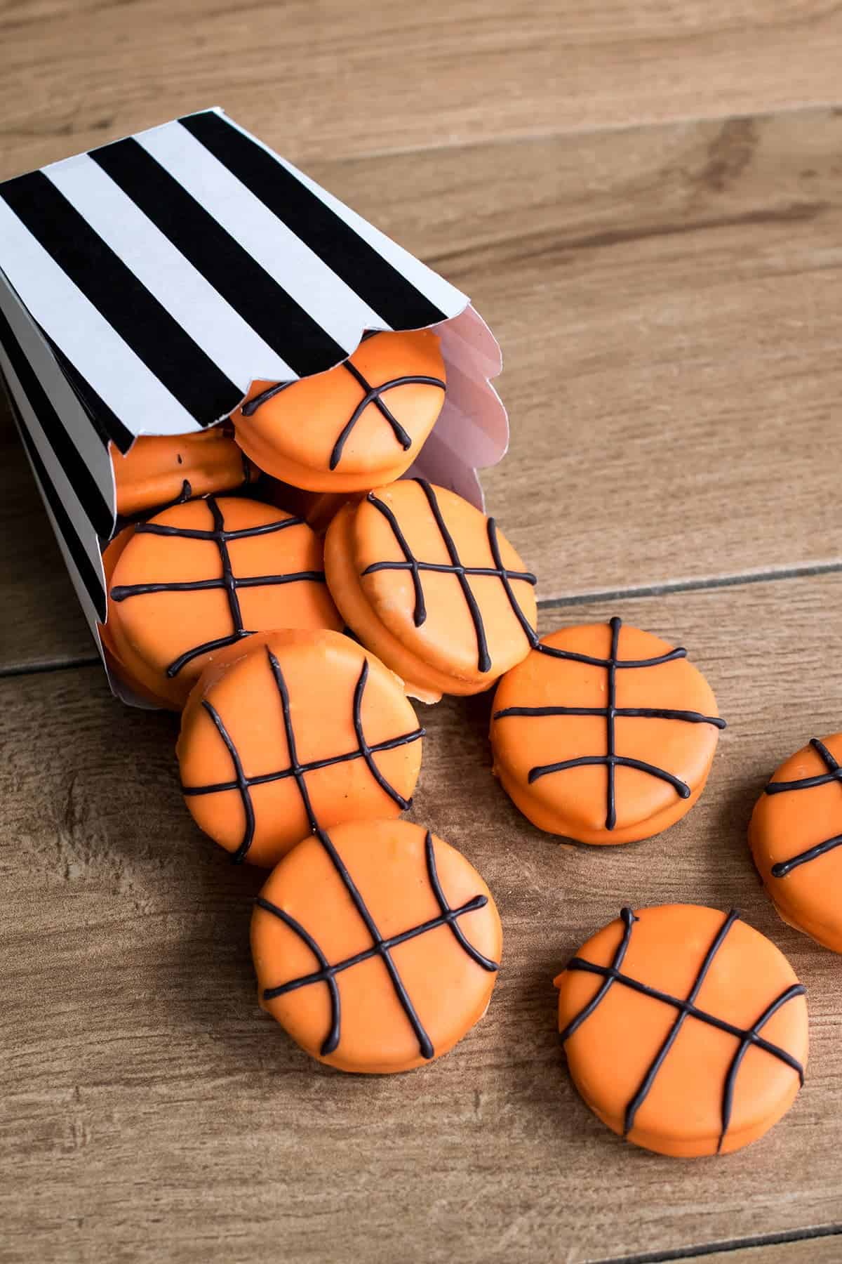 Chocolate Covered Oreo basketball cookies tipped onto wood table in black and white referee inspired container.