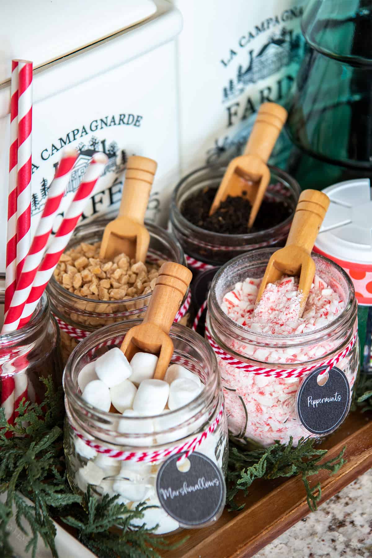 Christmas hot cocoa bar closeup with spoons in mason jars of marshmallows, mints, and candy bits.