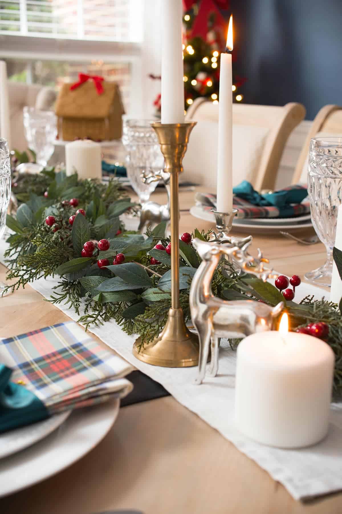Christmas table centerpiece made with tartan plaid, red berries, bay leaf garland, and reindeer.