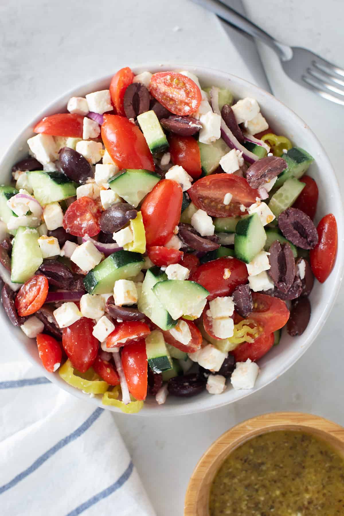 Greek salad filled with lettuce, kalamata olives, tomatoes, red onion, cucumbers, feta cheese in large white bowl.