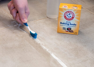 Man using a scrub brush for cleaning tile grout lines.