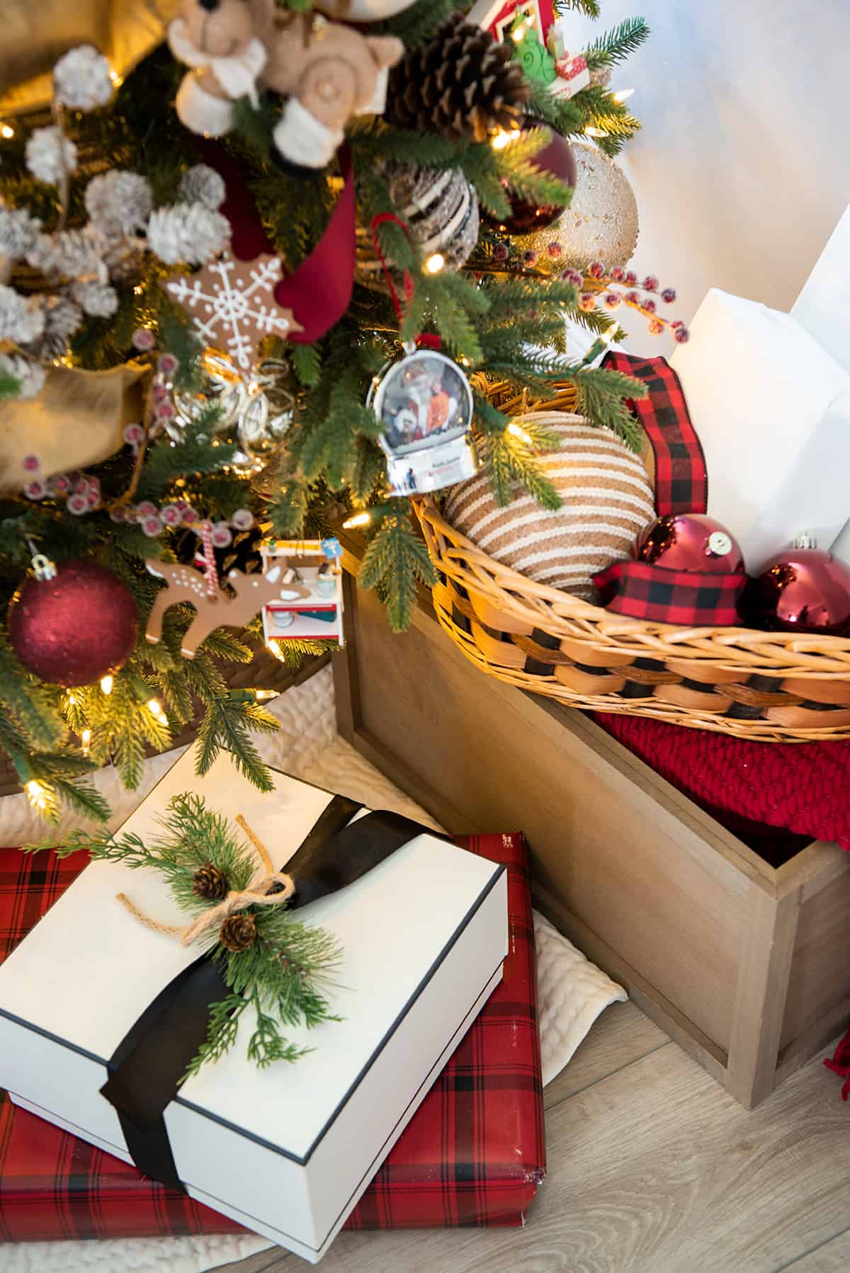 Closeup of decorations under the Christmas tree including a basket, ornaments, a blanket, and wrapped presents.