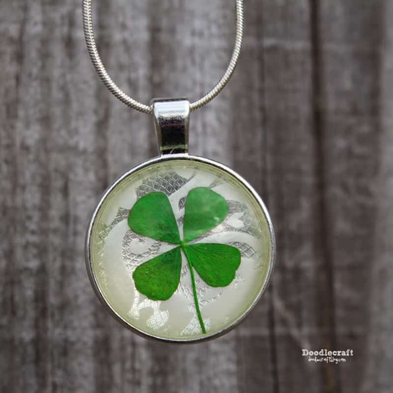 Lucky four leaf clover pendants hanging from chains in front of tree bark.