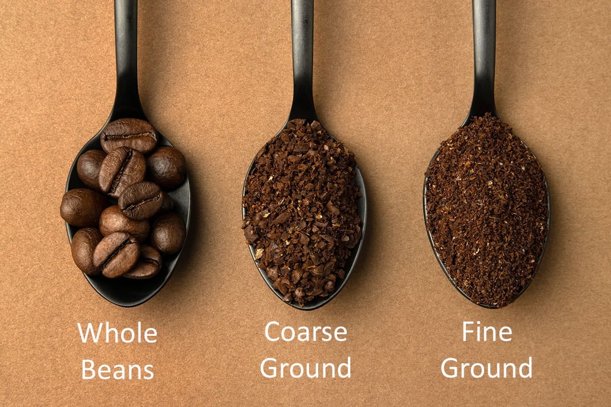 Three spoons displaying different coffee grind levels including whole beans, coarse ground, and fine ground.