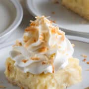 A slice of coconut cream pie bars on a plate with toasted coconut on top.
