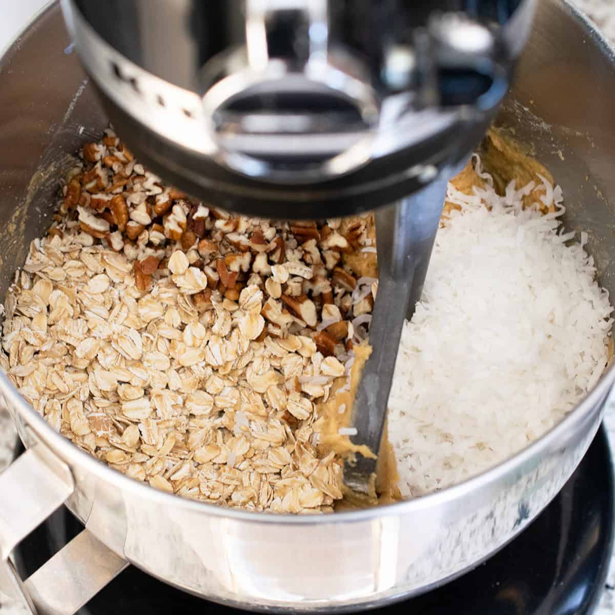 Chopped pecans, coconut, and oats in a stand mixer for making cookies.