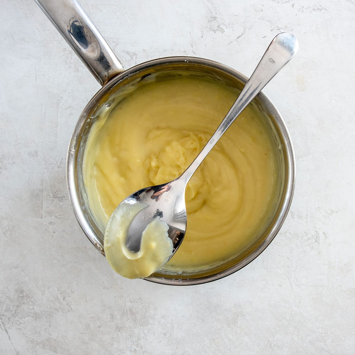 A saucepan with coconut cream filling and a spoon demonstrating how thick the custard is.