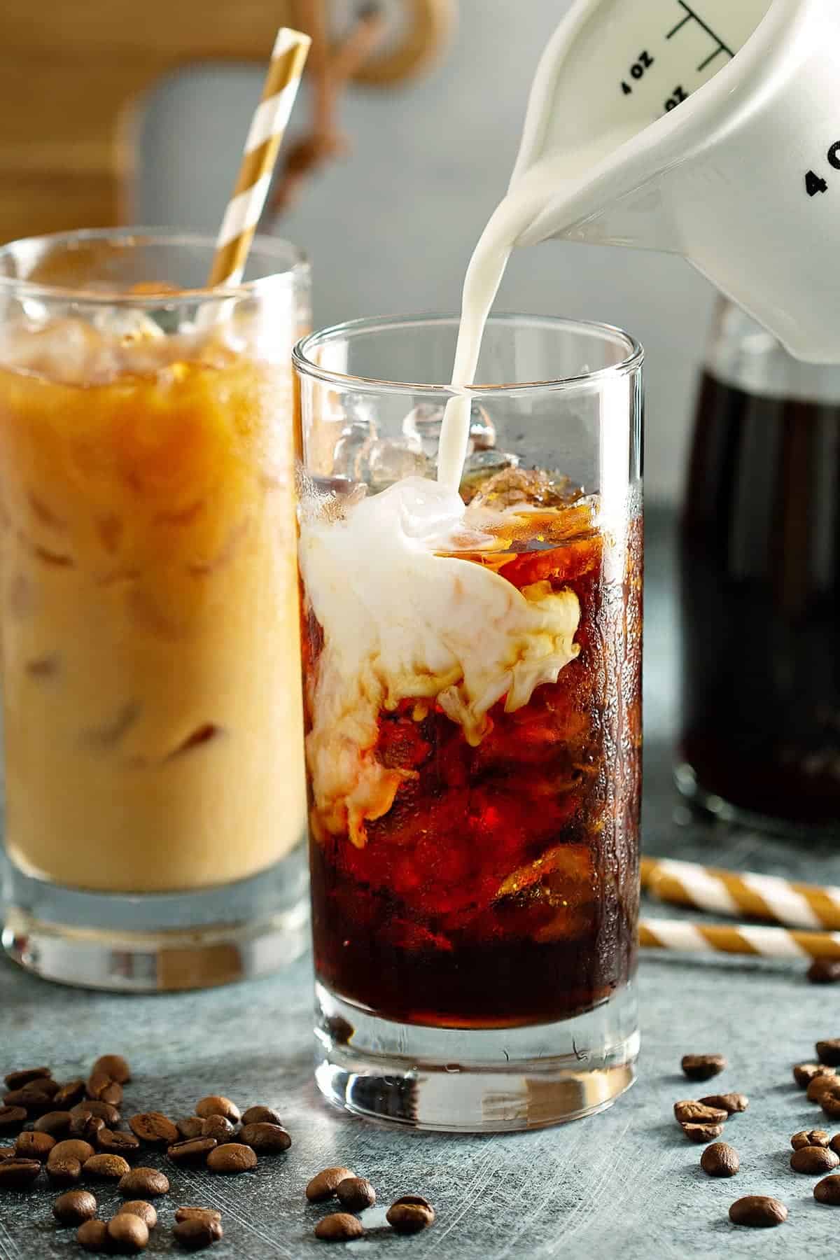 Cream pouring into a glass of cold coffee to make an iced latte.