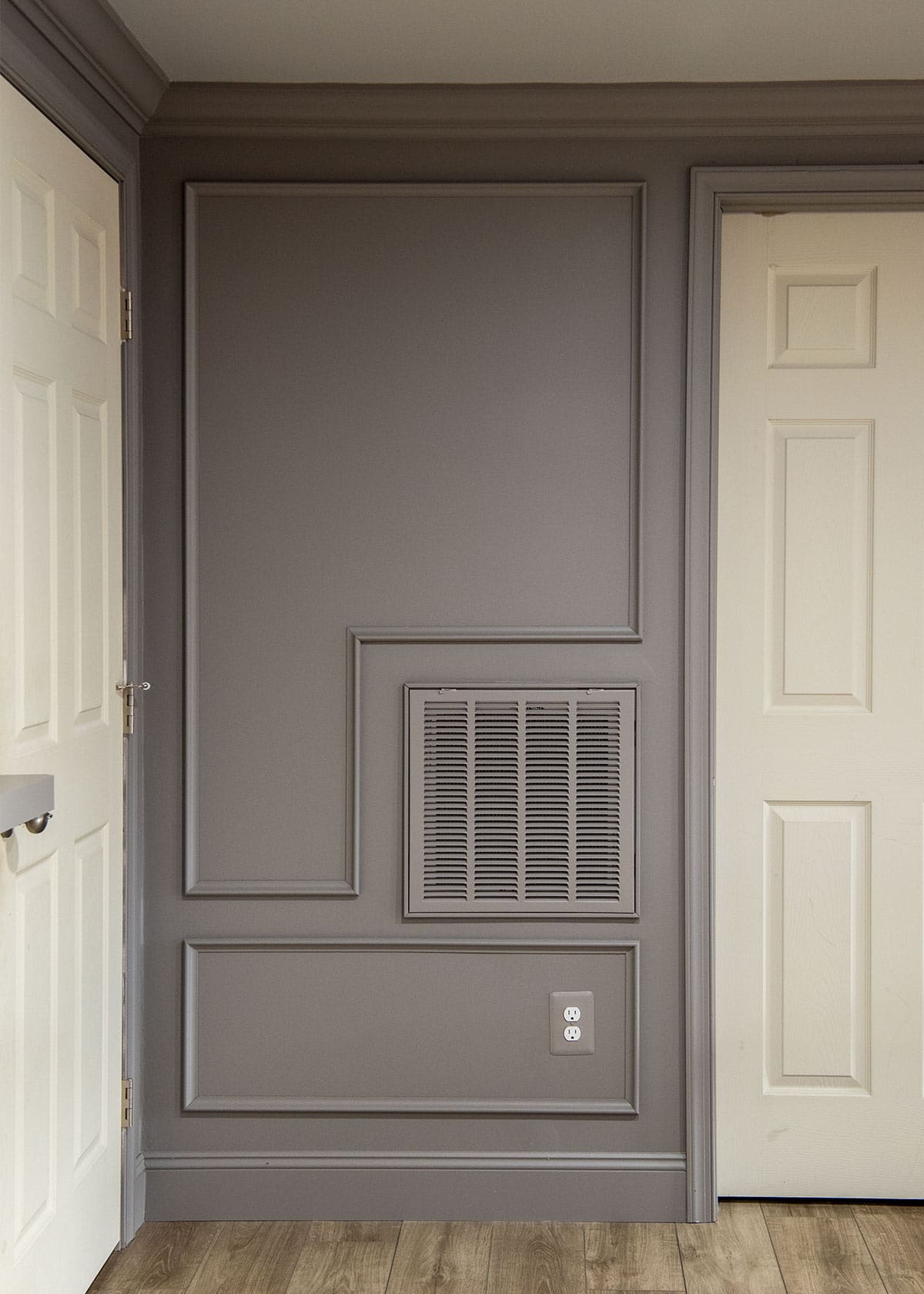 A grey wall with picture frame molding on it and a painted ventilation cover.