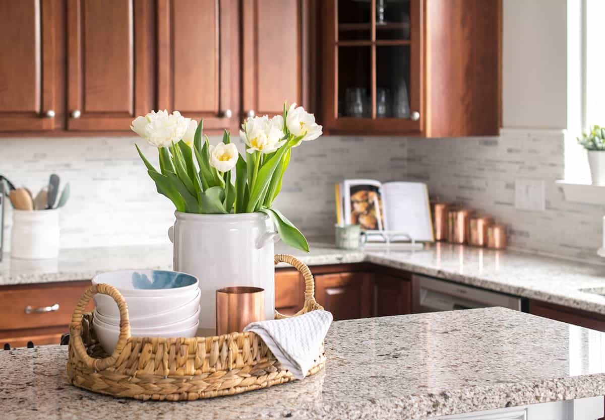 Marble breakfast bar with woven basket tray centerpiece filled with white peonies, bowls, and copper mug