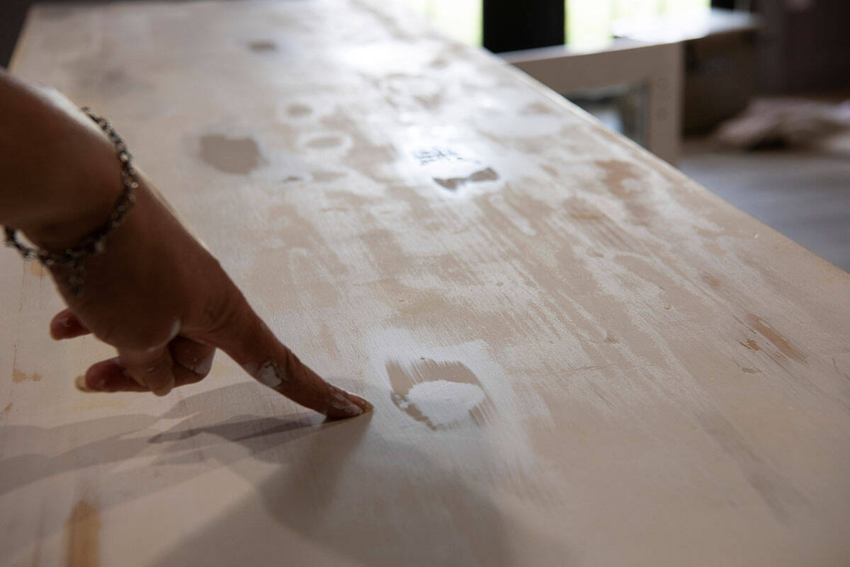 A woman pointing to a knot in knotty pine furniture that has been sealed with a shellac primer.