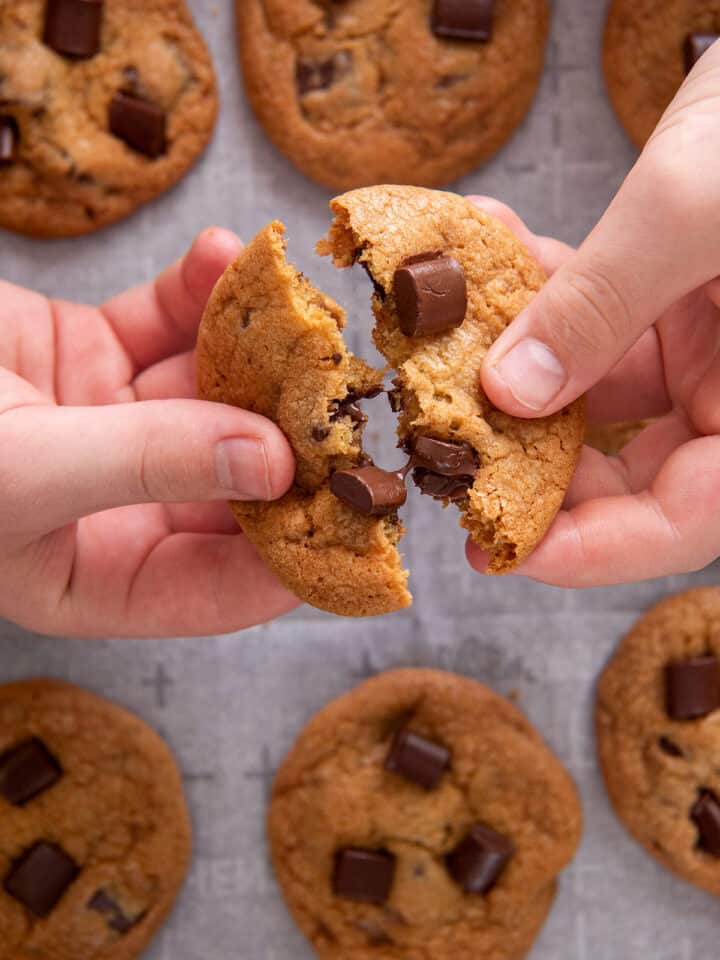 Hands holding up a toffee chocolate chip cookie and breaking it in half.