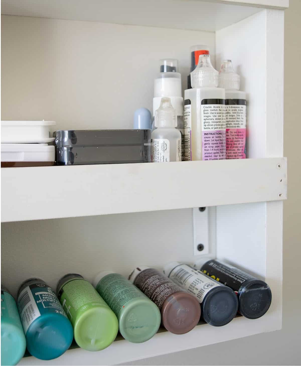 White painted DIY wall shelf stocked with craft supplies, paints, and stamps.
