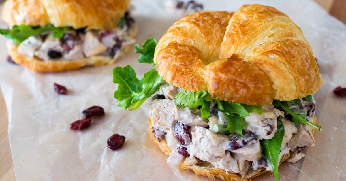 Cranberry Chicken Salad on a Croissant with greens and lunch wrap paper.