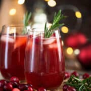 Sideview of christmas punch mocktails in wine glasses on a tray with ice and cranberries.