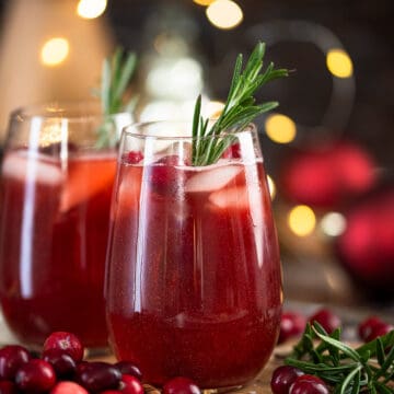 Sideview of christmas punch mocktails in wine glasses on a tray with ice and cranberries.