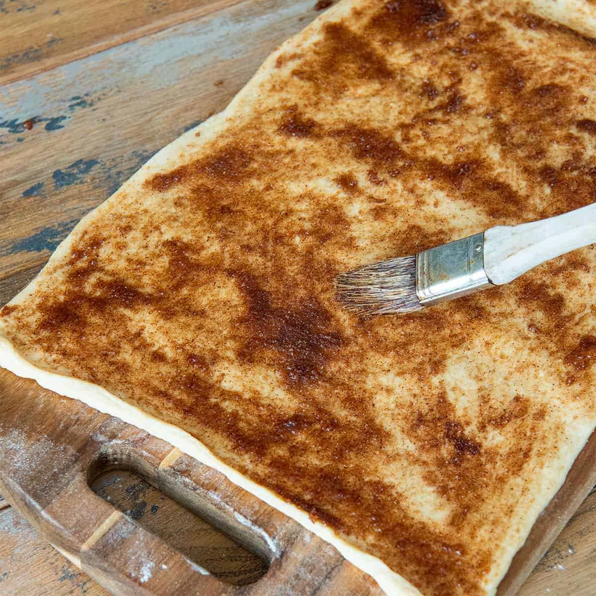 Dough with cinnamon sugar mixture being spread on by a brush.