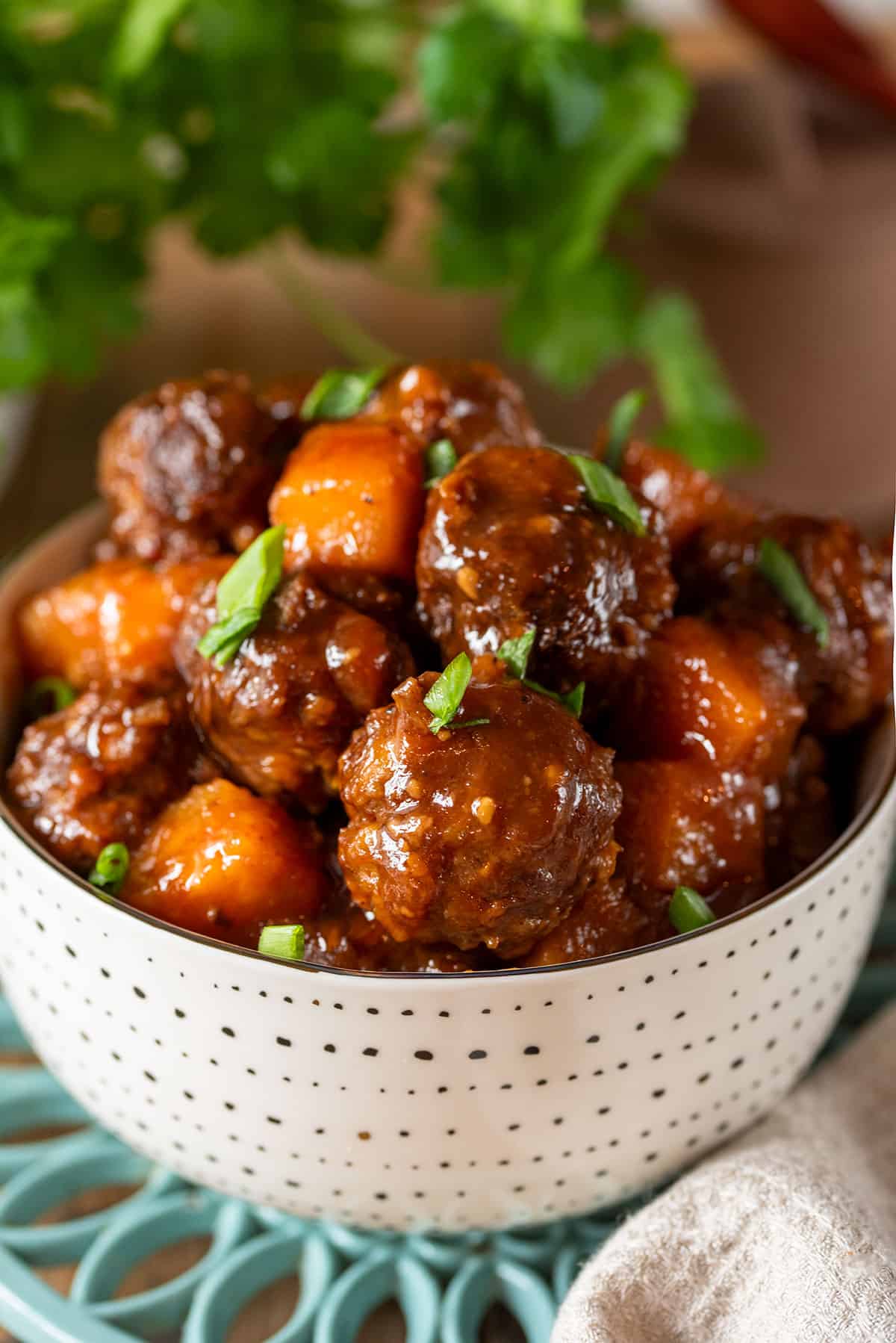 A bowl full of Hawaiian meatballs with a pineapple BBQ glaze and topped with green onions.