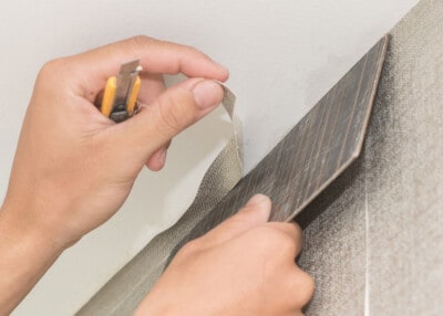 Hands using a smoothing tool and a razor knife to remove excess paper from wall.