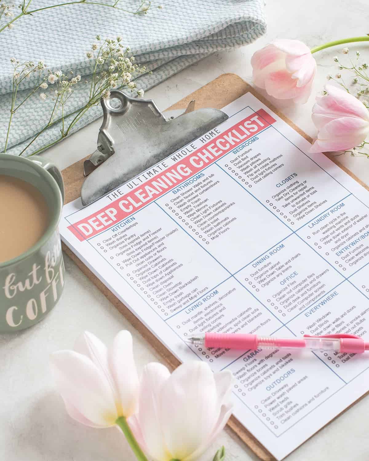 Whole Home Cleaning Printable Checklist on clipboard with pink pen. Norwex cloth, baby's breath, pink tulip and coffee cup in background.