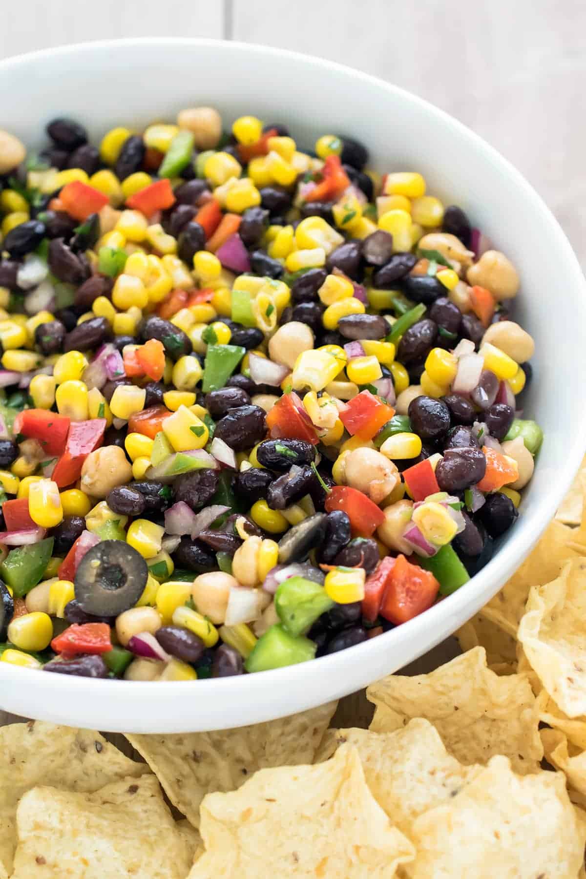 Heaping bowl of chopped salad with beans, corn, cilantro, fresh chopped veggies, olives, and vinaigrette.