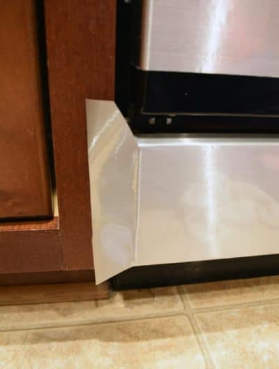 Faux stainless steel contact paper applied to bottom of black dishwasher with view of how to apply around corner.