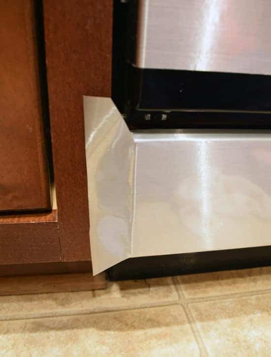 Faux stainless steel contact paper applied to bottom of black dishwasher with view of how to apply around corner. 