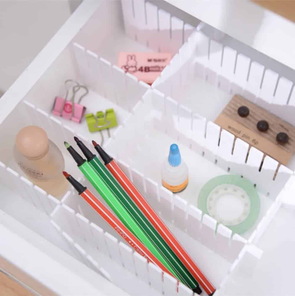 White drawer divider with compartments containing office items such as pens, paper clips, tape and wood push pins.