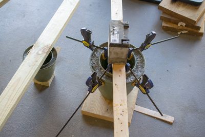 Two planters filled with concrete mix to create cement plant pots. The inner mold is held down with boards and clamps.