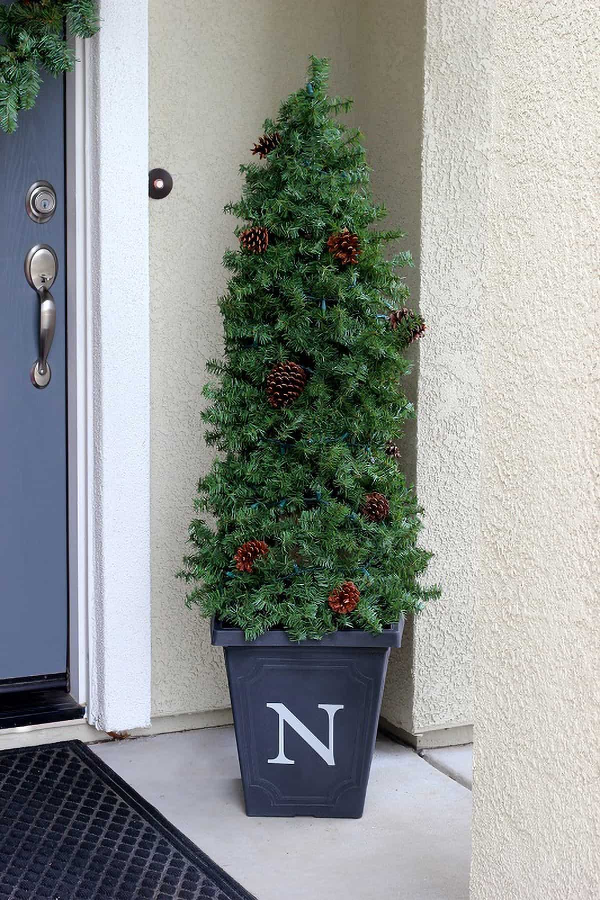 DIY lighted evergreen topiary in a bucket in front of a door.