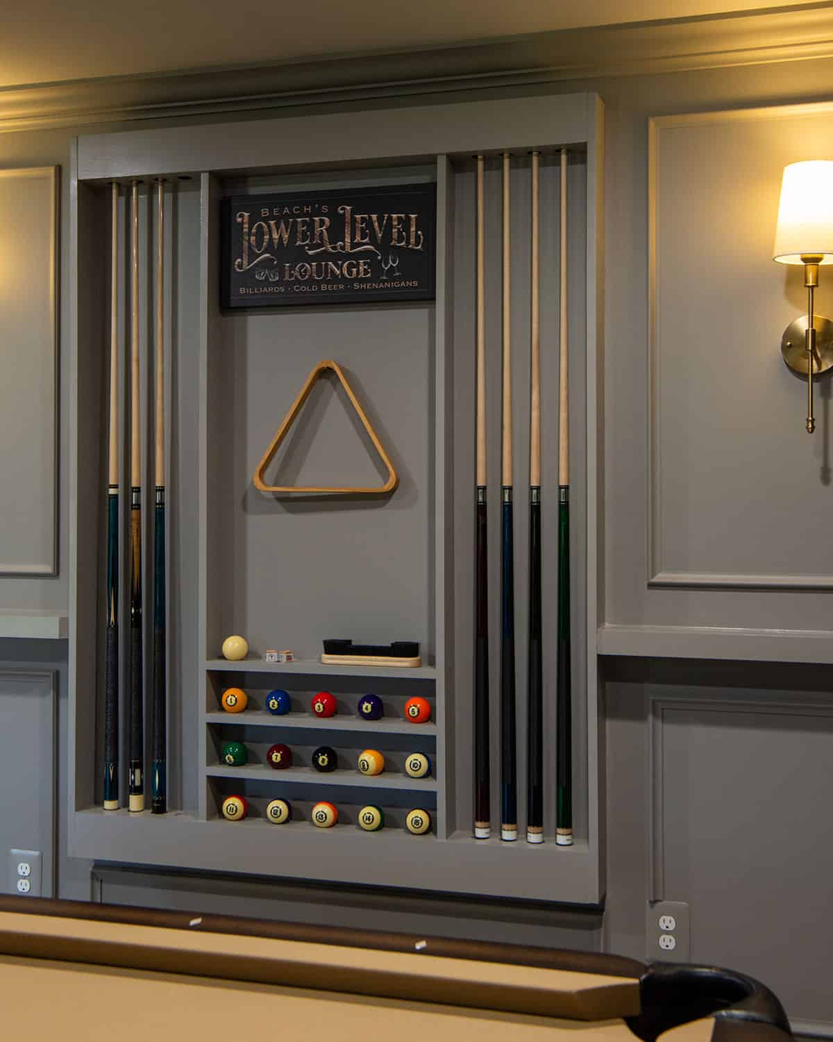 A custom pool cue rack built onto the wall with pool balls, a custom sign, and cues on either side.