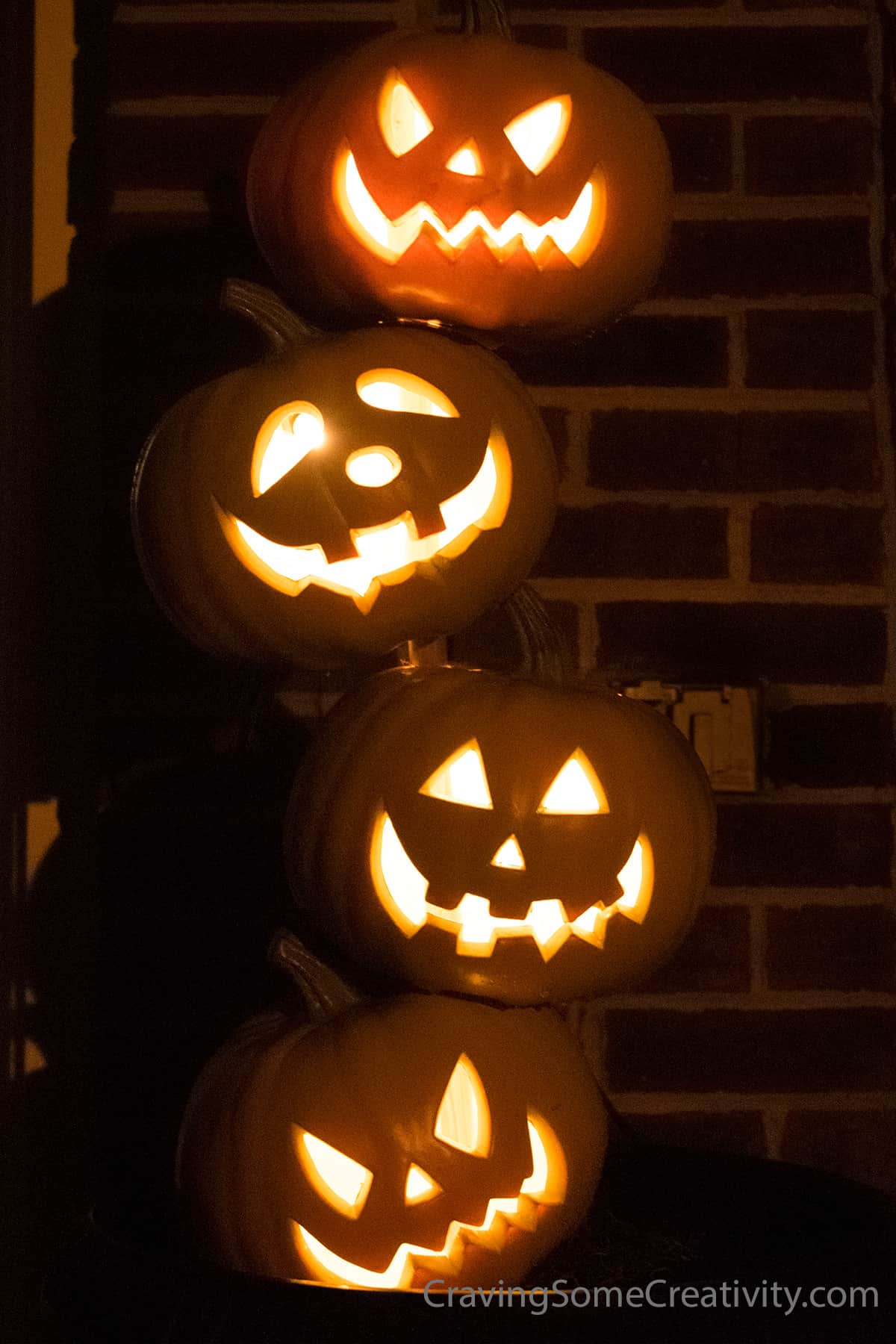 Jack-o'-lanterns stacked on a diy pumpkin topiary and lit up for the night.