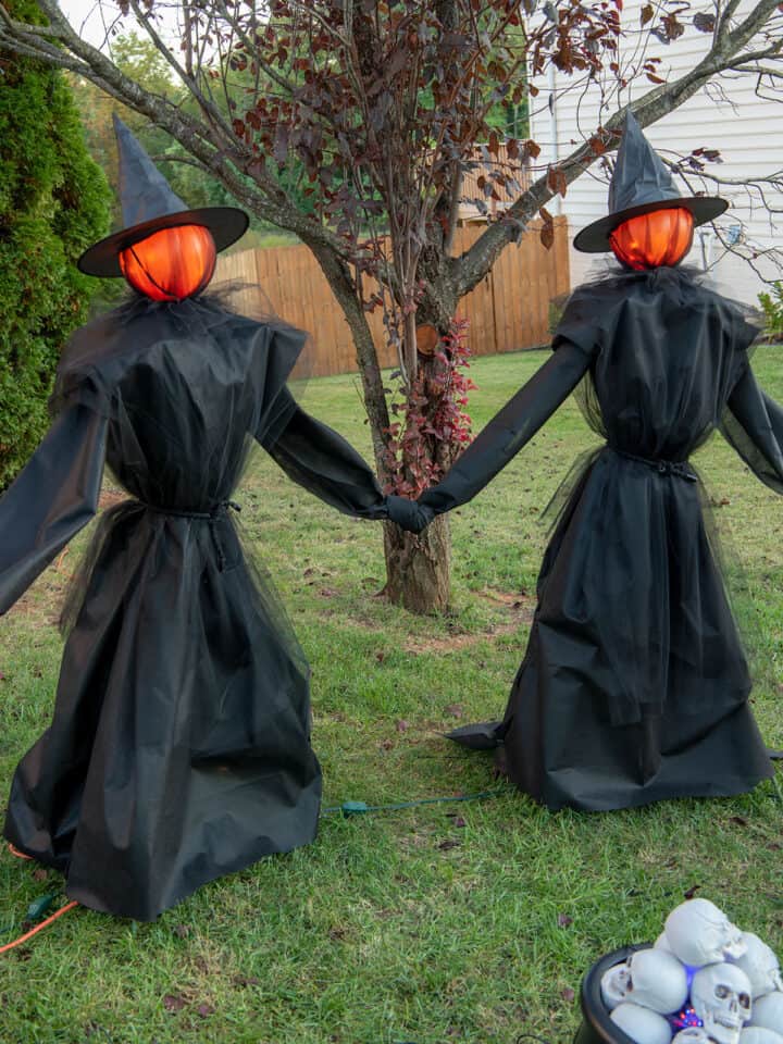 Two DIY witches with glowing heads standing near a cauldron filled with skulls.