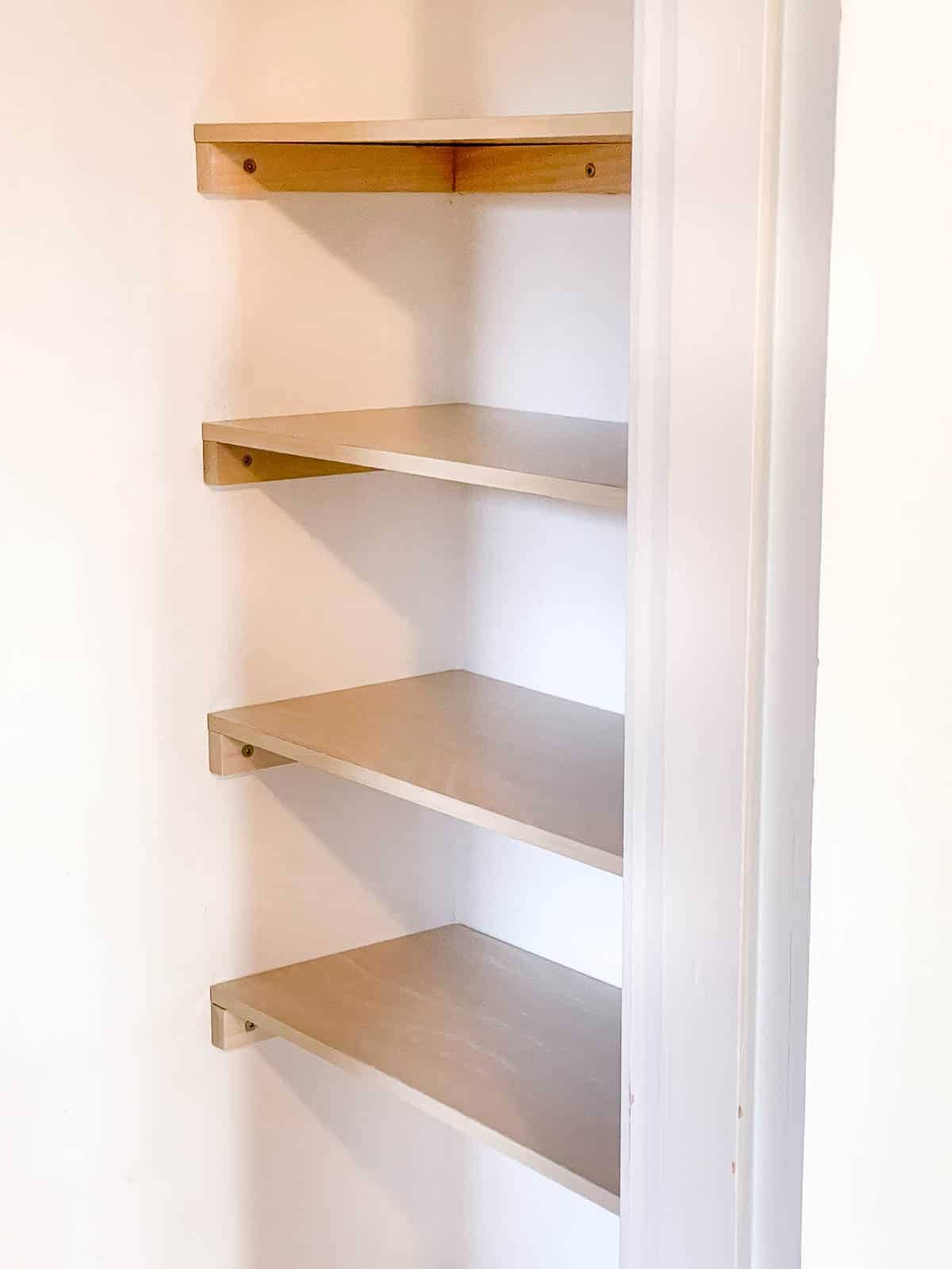 Empty white closet with custom built wood shelves for a laundry room.