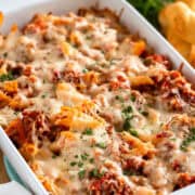 A casserole pan of sausage and penne pasta in a red sauce with melted mozzarella cheese on top.