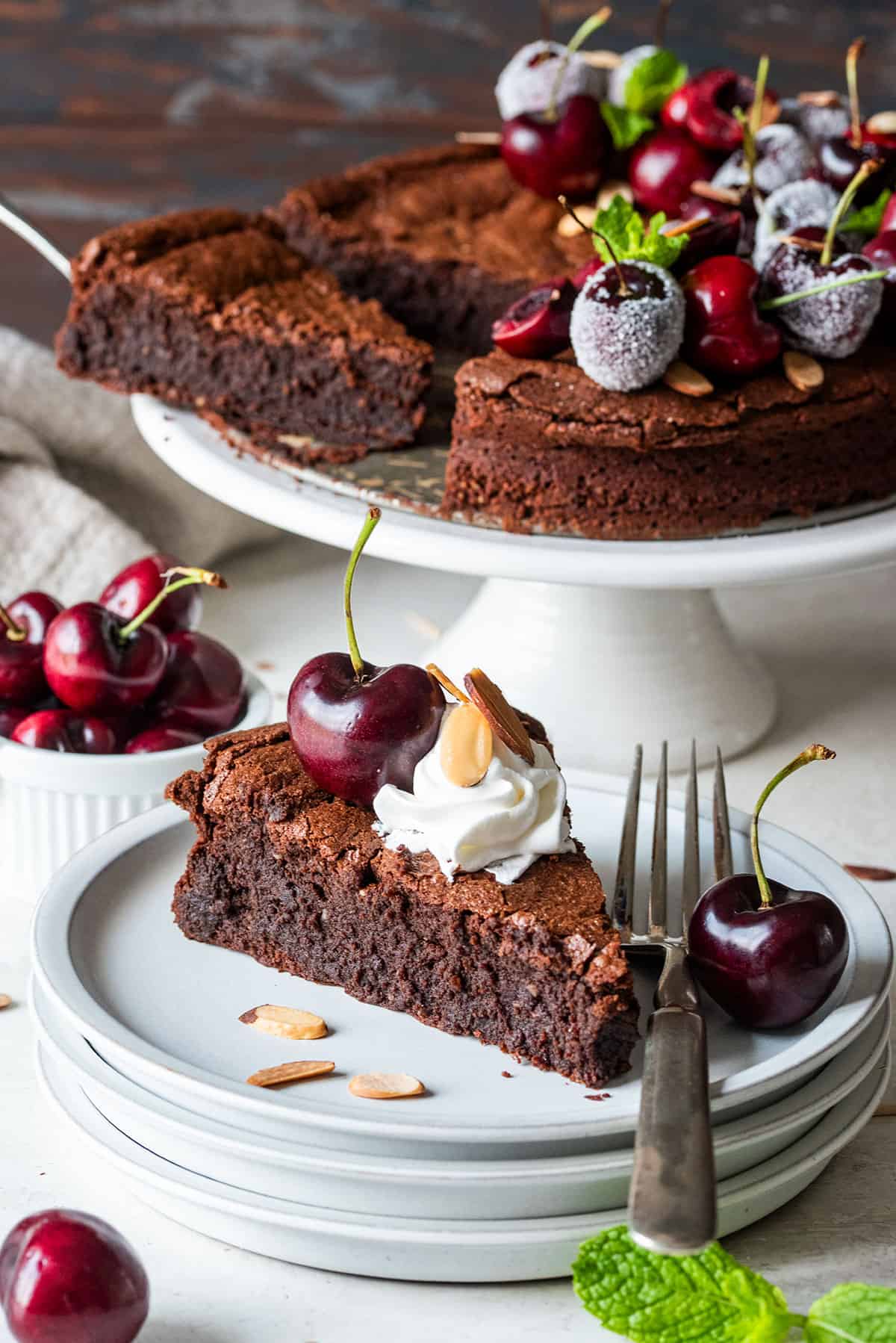 A slice of flourless chocolate cake on a plate topped with cherries and whipped cream.