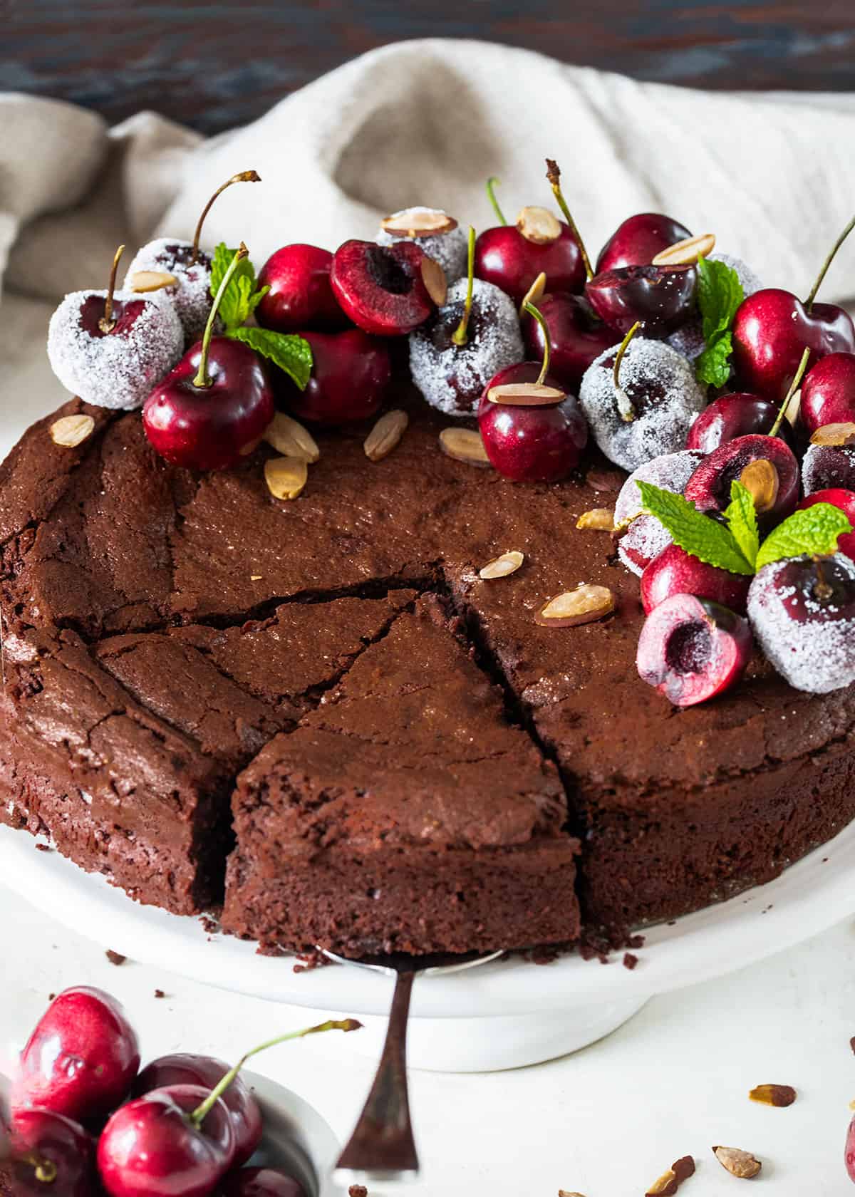 A chocolate brownie cake topped with sugared fresh berries being cut and served.