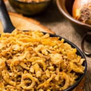 Fried onion strings in a cast iron pan with wood background..