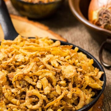 Fried onion strings in a cast iron pan with wood background..
