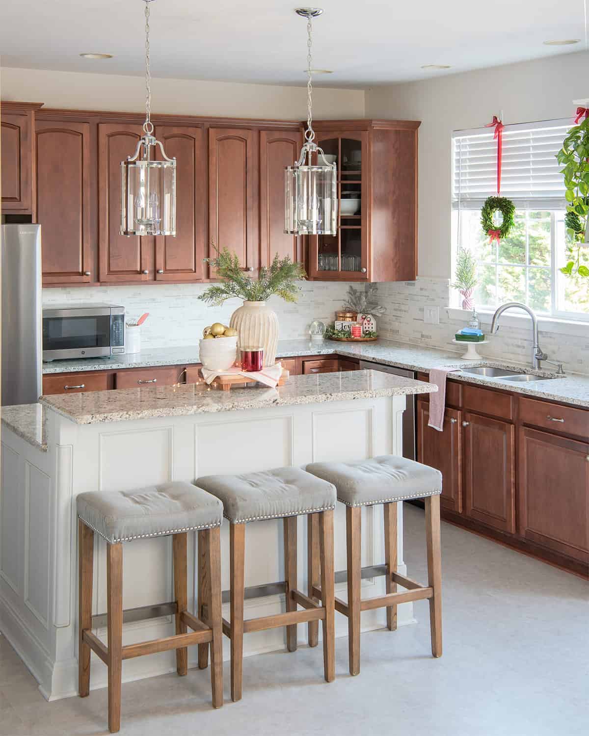 Christmas kitchen decorated for holidays with vignettes on large island and stools in front of dark cabinets.