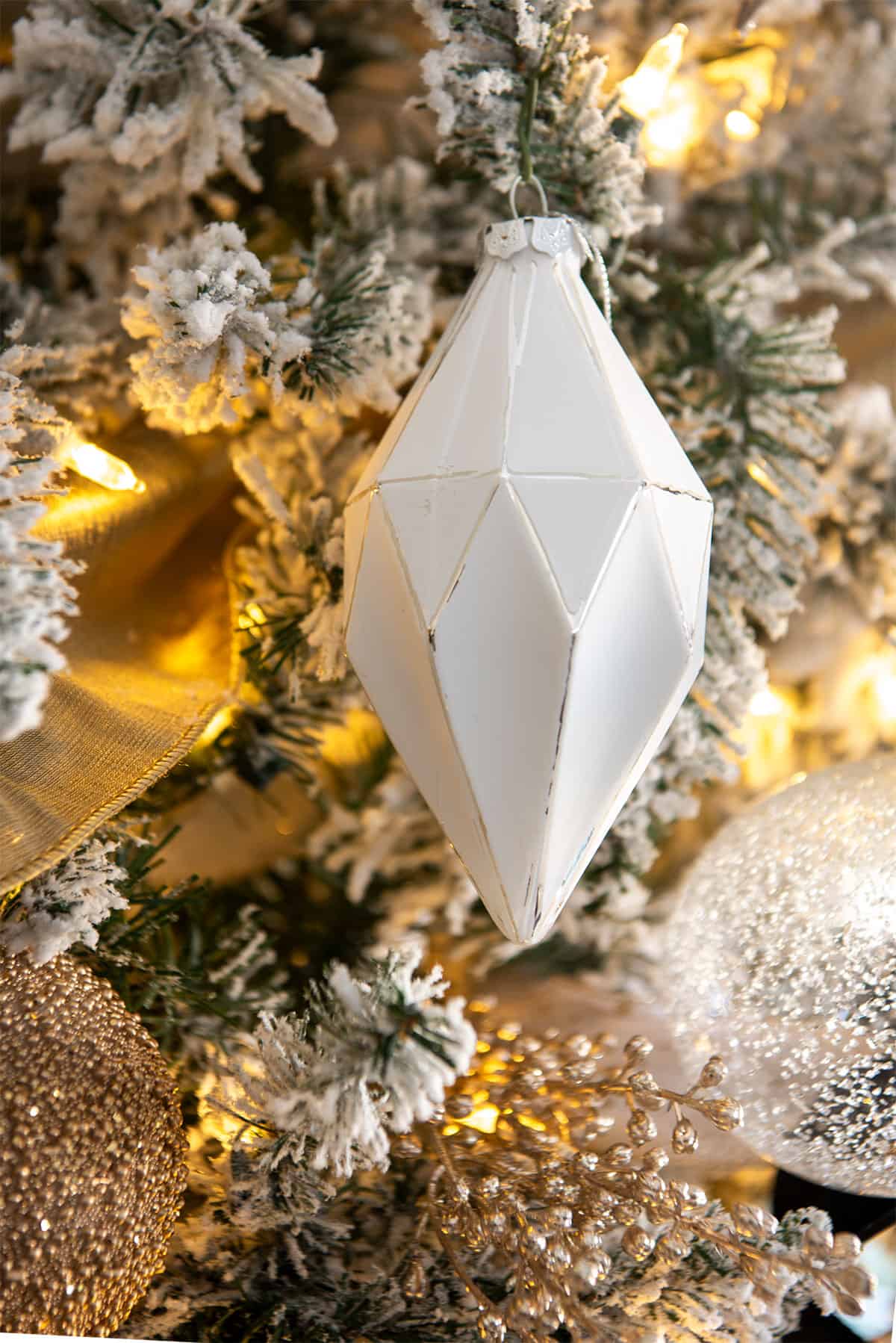 Closeup of a geometric tapered white ornament on a flocked silver Christmas tree.