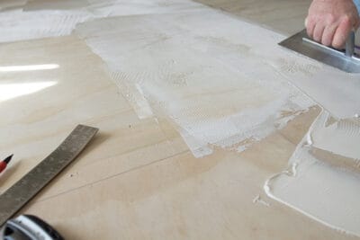 Glue down vinyl tile being installed with the adhesive being spread on the floor.