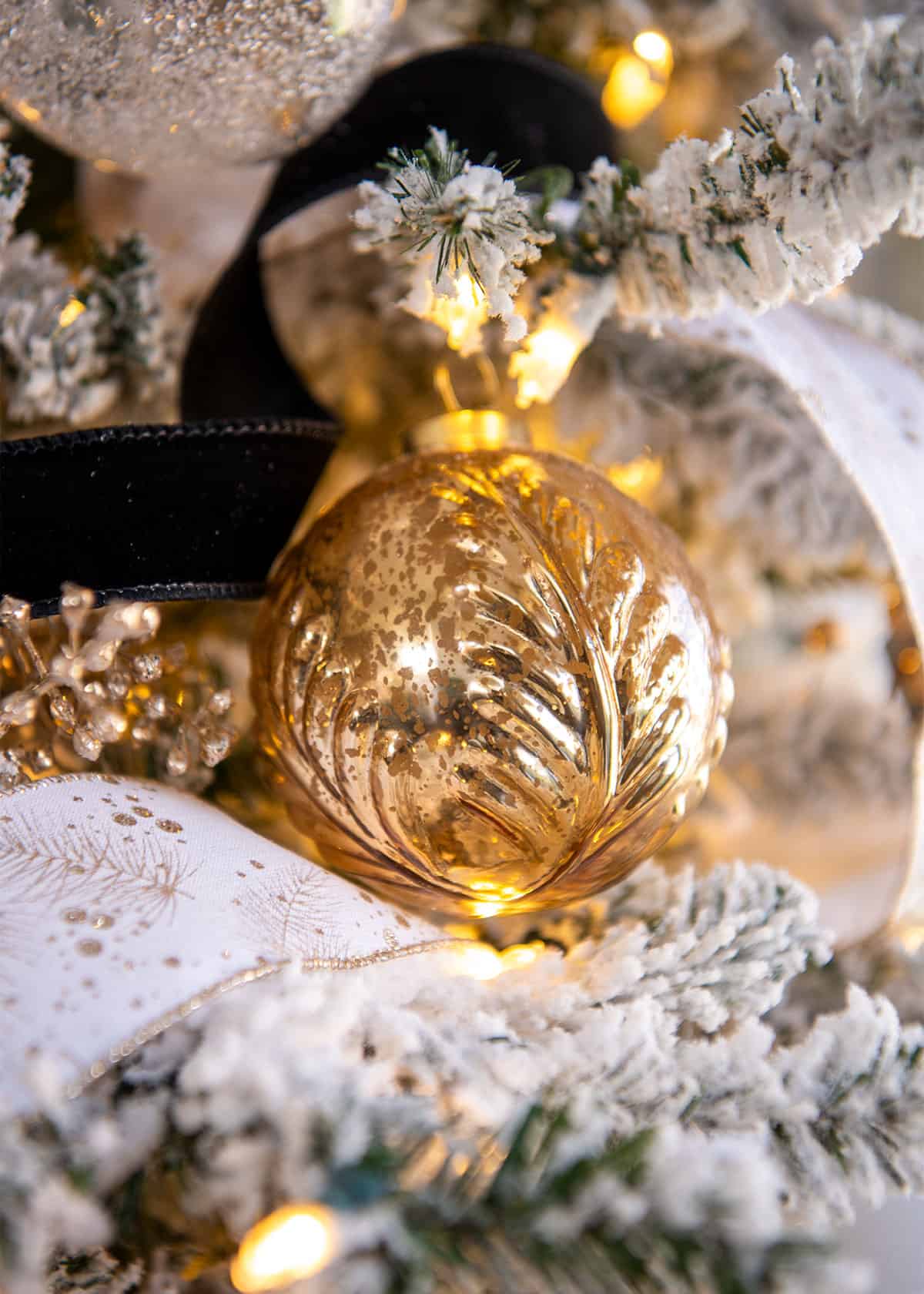 Closeup of a mercury gold ball glass ornament with Christmas lights around it.