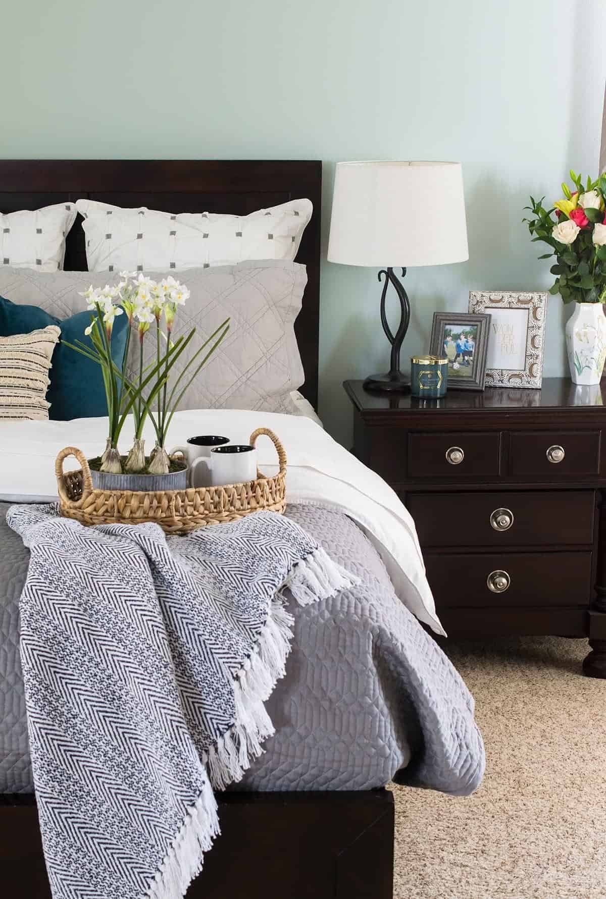 Green master bed made up. Gray and white color scheme with blanket and basket for welcoming guests.