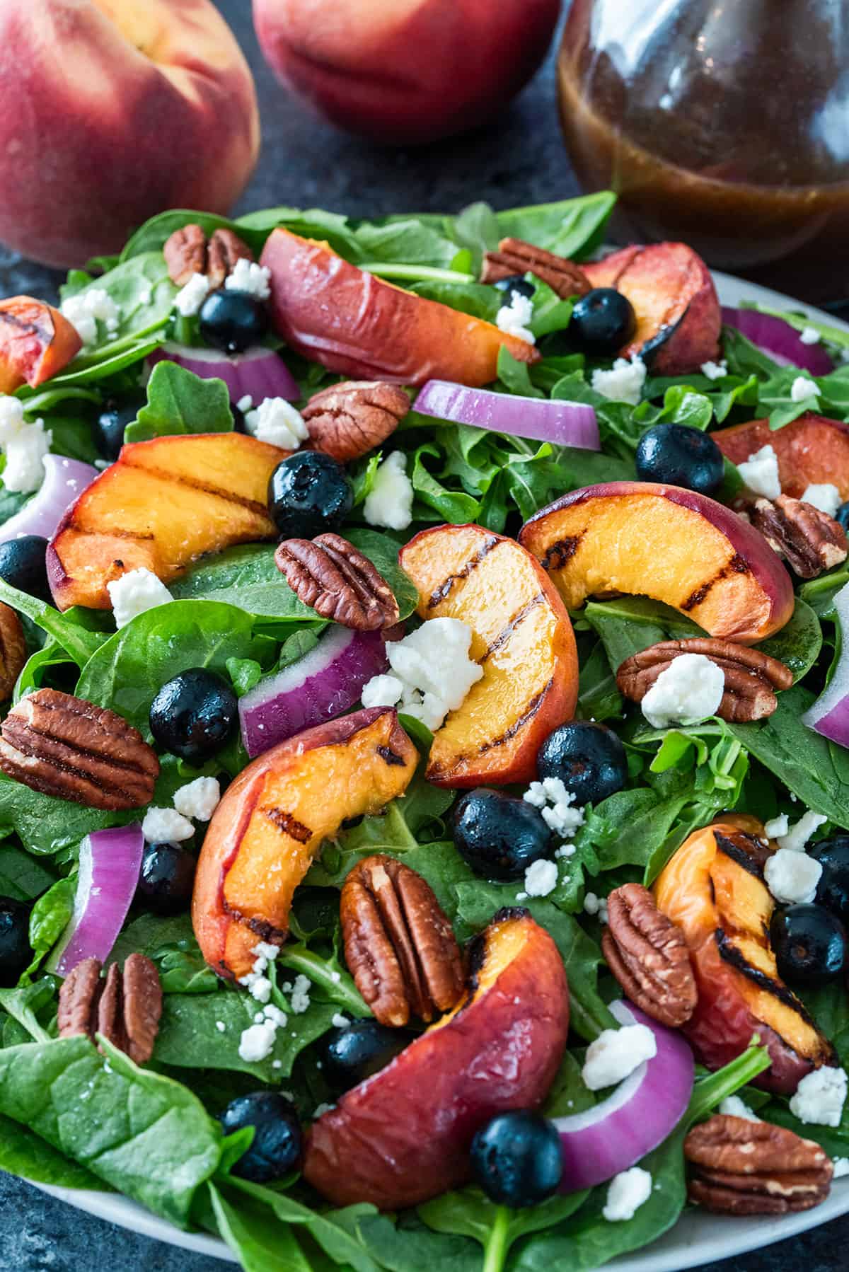 Spinach salad with grilled peaches, blueberries, cheese, pecans, and red onions on a plate.