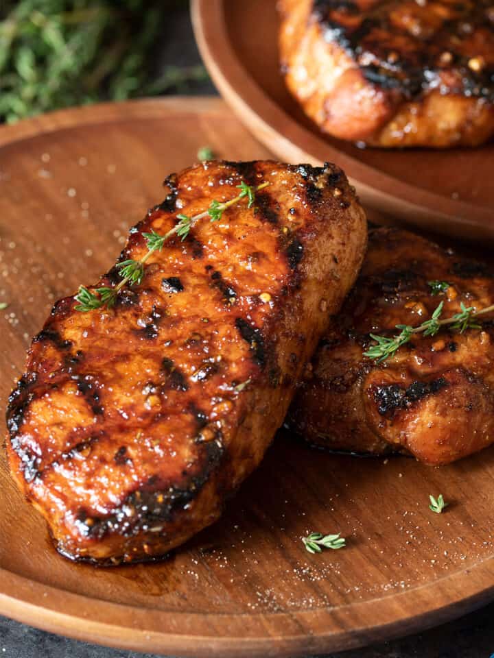 Two grilled pork chops with grill marks laid out on a wooden background.