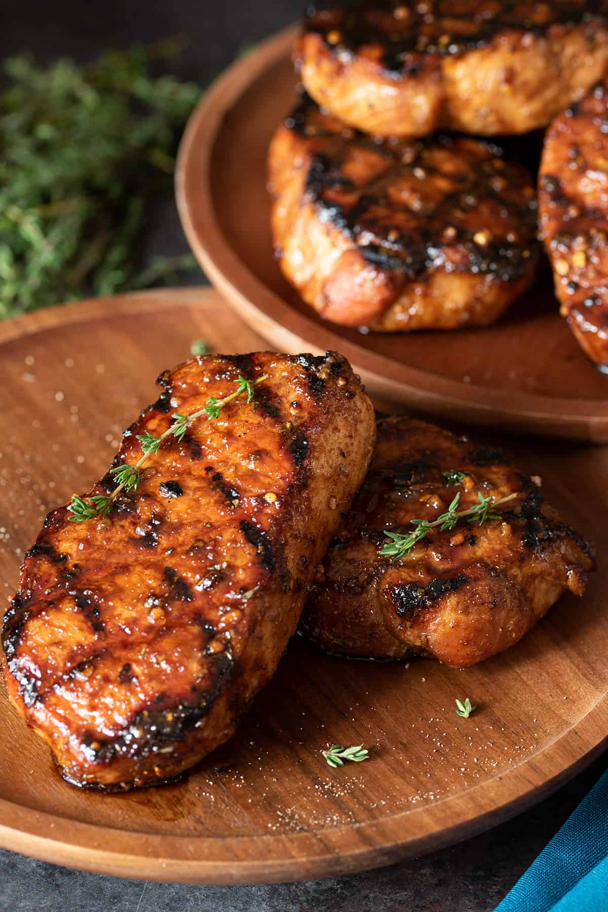 Two grilled pork chops stacked on a serving plate with thyme sprigs on top.