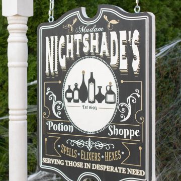 Halloween yard sign with witch's apothecary shop motif hanging on a frame.