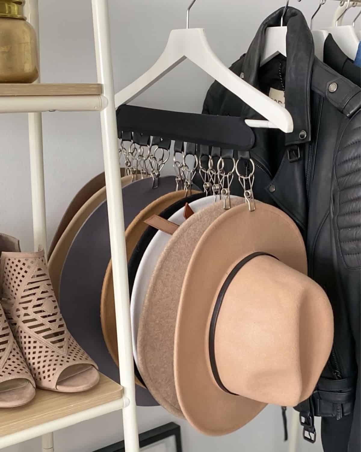 Hats hanging off a hanger via a clip mechanism in a white closet.