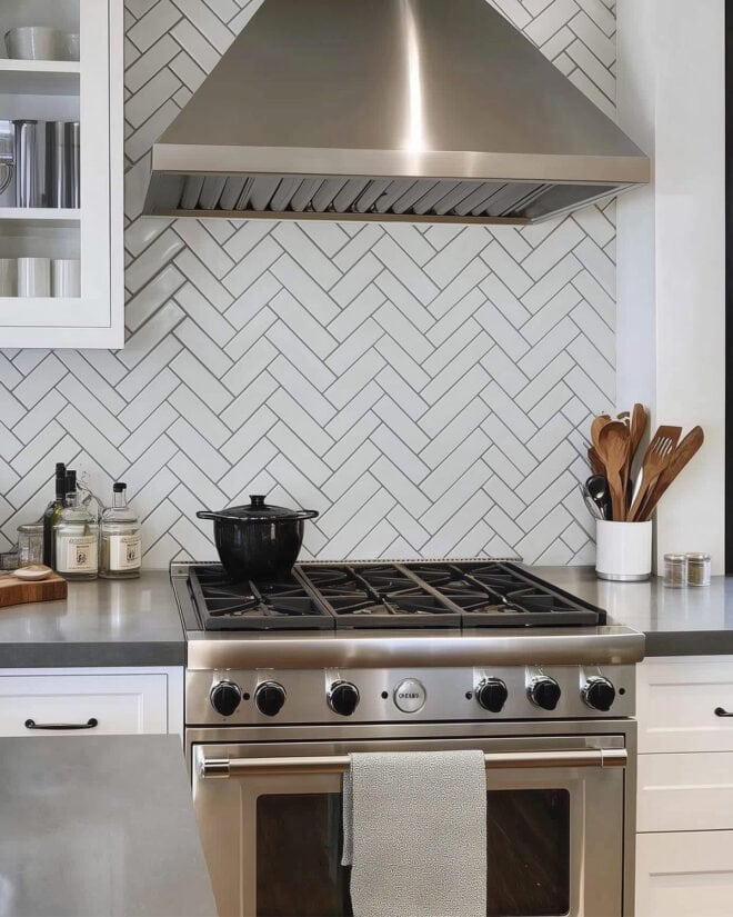 Grey kitchen with herringbone tile pattern backsplash over grey countertops.